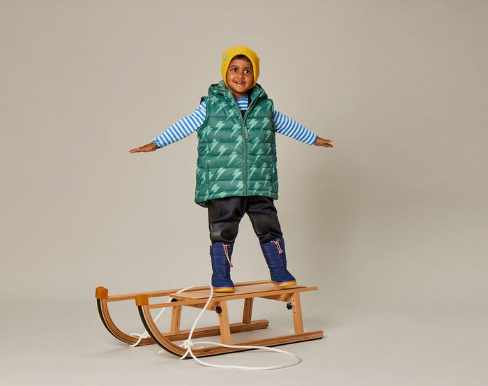 Child on sled wearing sleeveless Snapper Rock - 2 in 1 Puffer Jacket & Vest - Lightning Bolt - Available at www.tenlittle.com