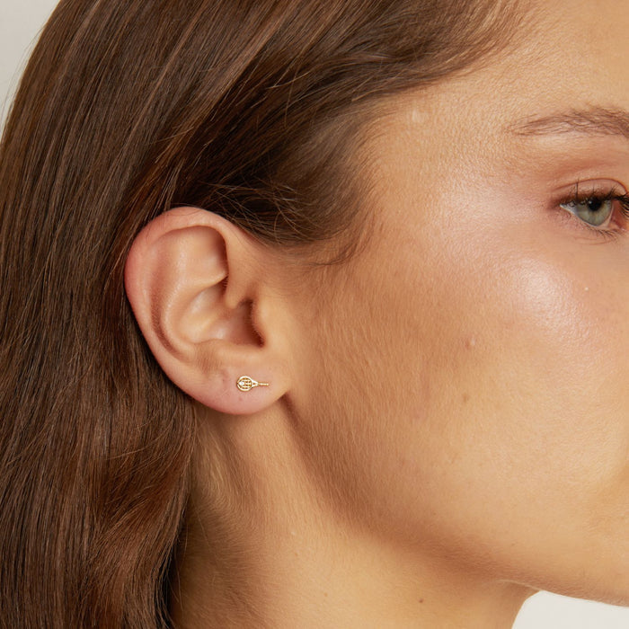 Model. Close-up of an ear wearing a gold earring with a tennis racket design.