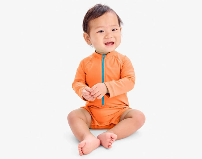 Baby sitting wearing Primary Baby One-Piece Rash Guard - Cantaloupe. Available at www.tenlittle.com