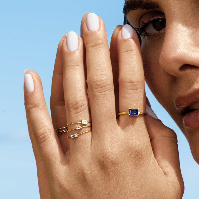 Model Close-up of a hand wearing three gold baguette rings against a light blue background