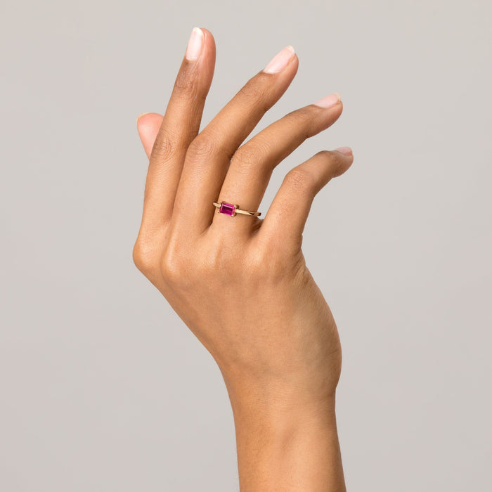 Model Close-up of a raised hand wearing a gold ring with a pink baguette gemstone against a light grey background