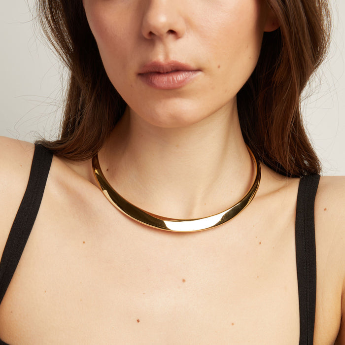 Model. Close up of thick cold collar necklace on woman with neutral background.