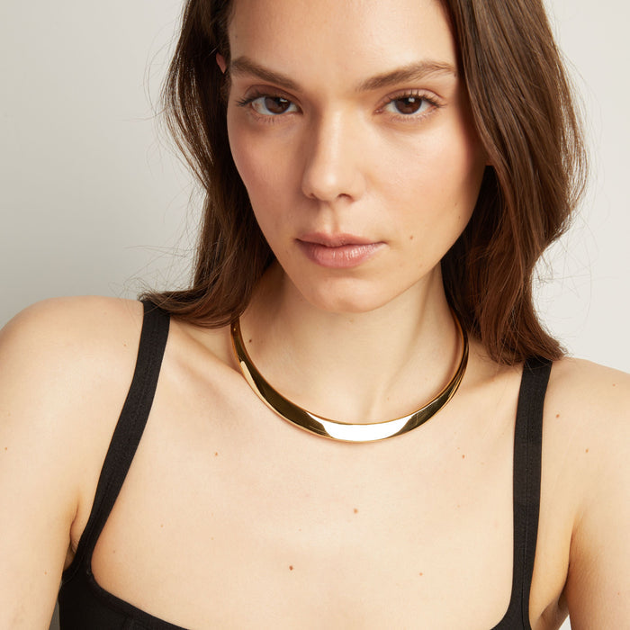 Model. Close up of thick cold collar necklace on woman with neutral background.