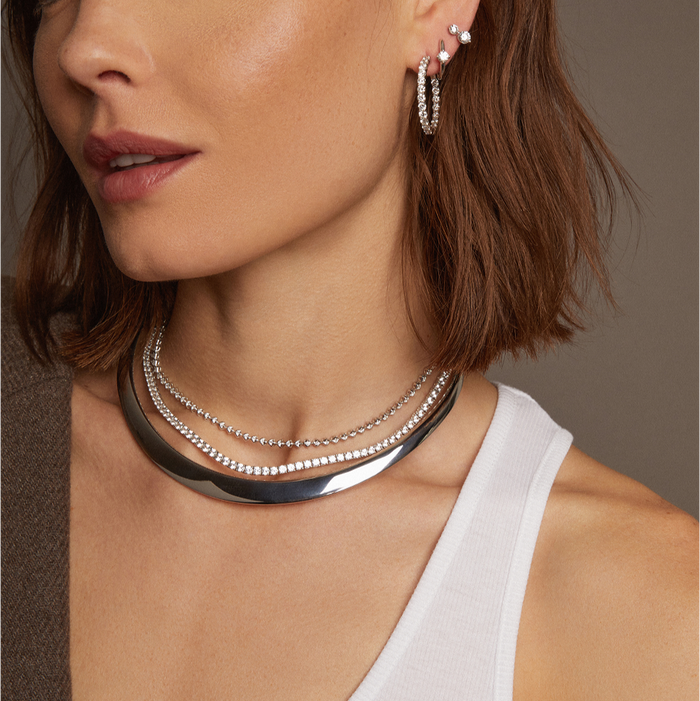 Model. Woman wearing a brown blazer and white top with layered necklaces against a neutral background