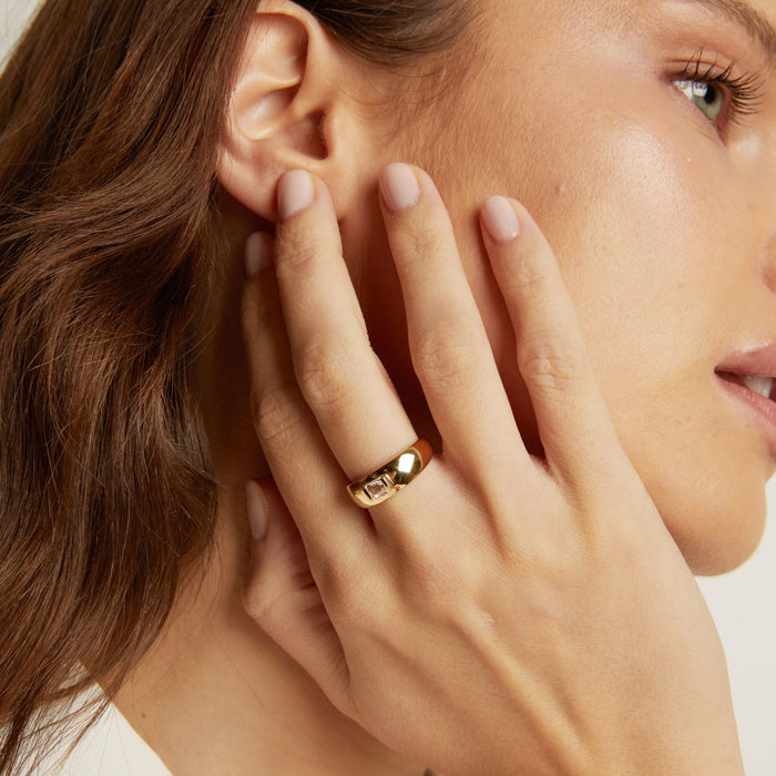 Model. Close-up of a woman wearing a gold ring on her finger, touching her ear.