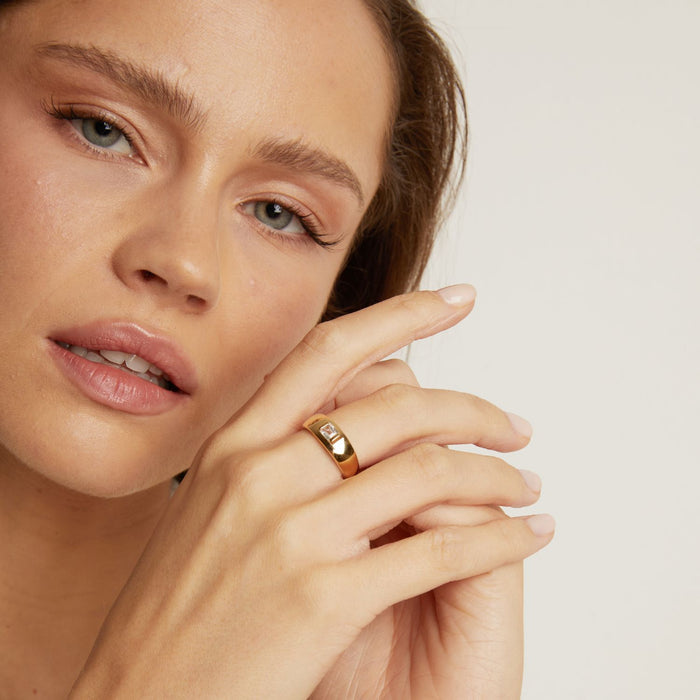 Model. Close-up of a woman's face with a gold ring on her finger against a neutral background