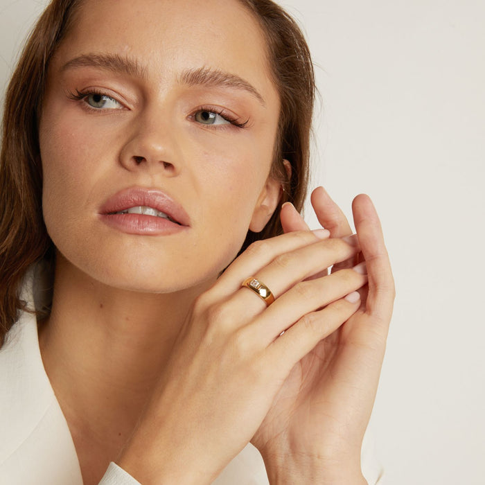 Model. Woman wearing a gold ring on a neutral background
