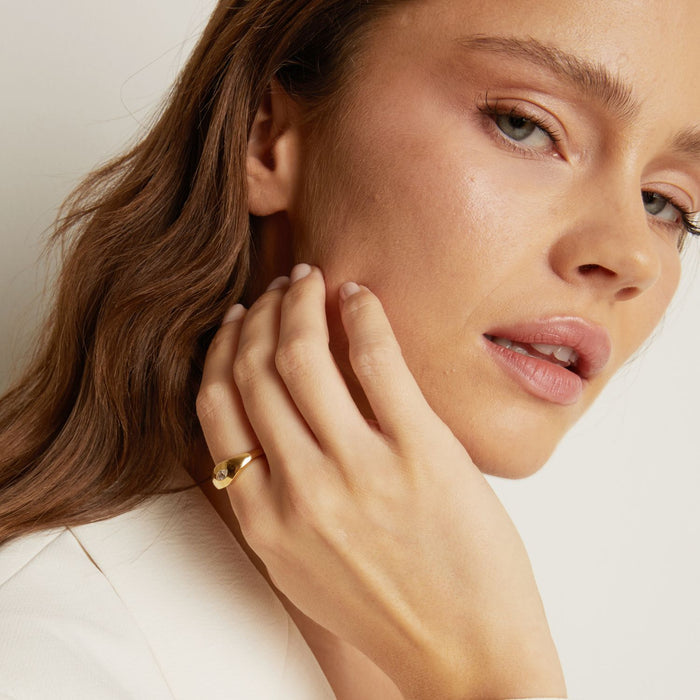 Model. Close-up of a woman wearing a gold earring and ring on a neutral background