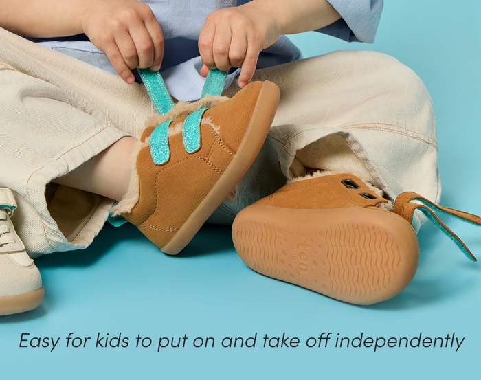 Child putting on Ten Little Cozy Suede Sneakers, easy for kids to put on and take off independently - Toffee Brown. Available at www.tenlittle.com