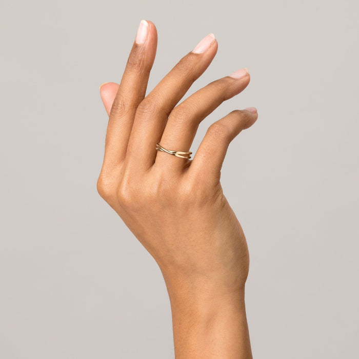 Model Close-up of a hand posed gracefully against a light grey background, showcasing a classic solid gold crossover ring.
