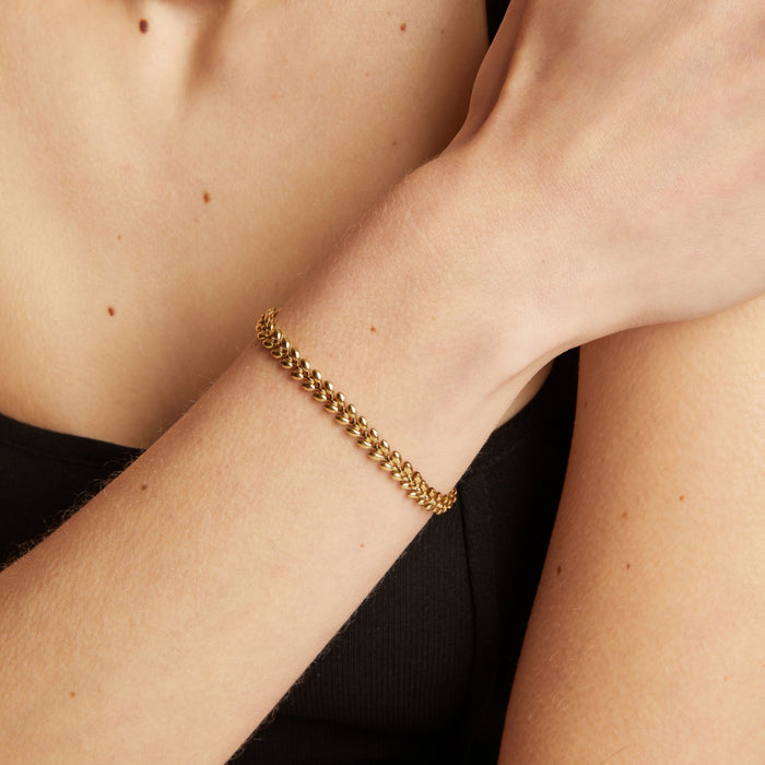 Model. Gold chain bracelet on a person's wrist with a neutral background.
