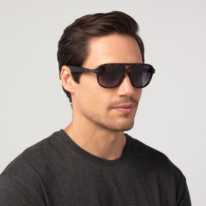 A man with short dark hair, wearing Eddie Bauer Explorer smart glasses and a dark gray t-shirt, poses against a plain light background.