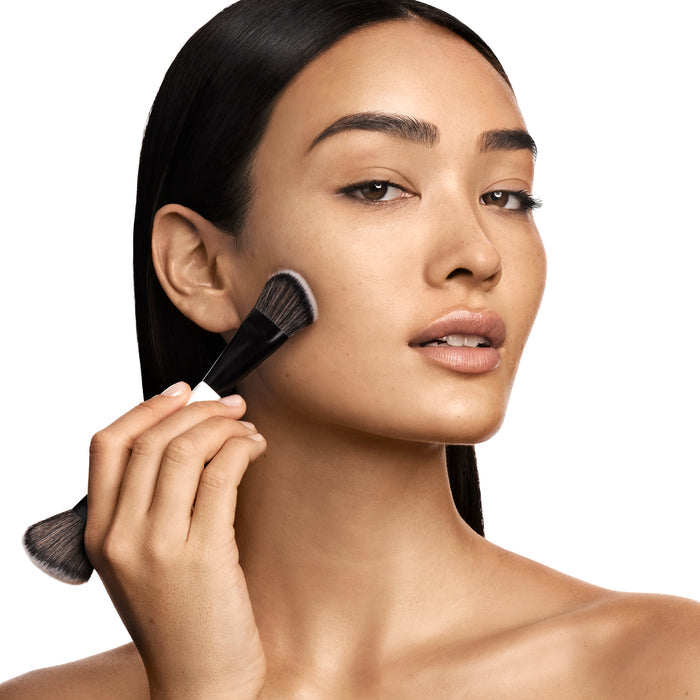 A model applying foundation on her face using Makeup By Mario's F4 Dual-Ended Foundation and face brush.