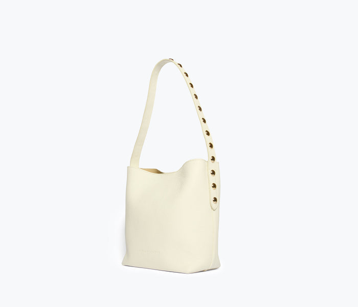 Freda Salvador Fiona Small Studded Tote bag in bone color with gold studs, side view showing sleek leather design and compact size.
