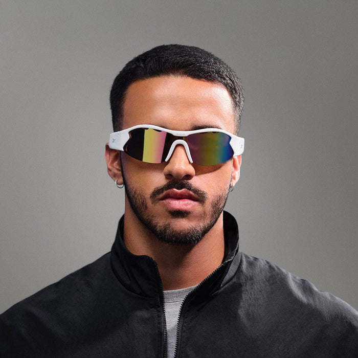 A man with short dark hair, a trimmed beard, and mustache wears Reebok Flash audio sunglasses with white frames and a black jacket against a plain gray background.