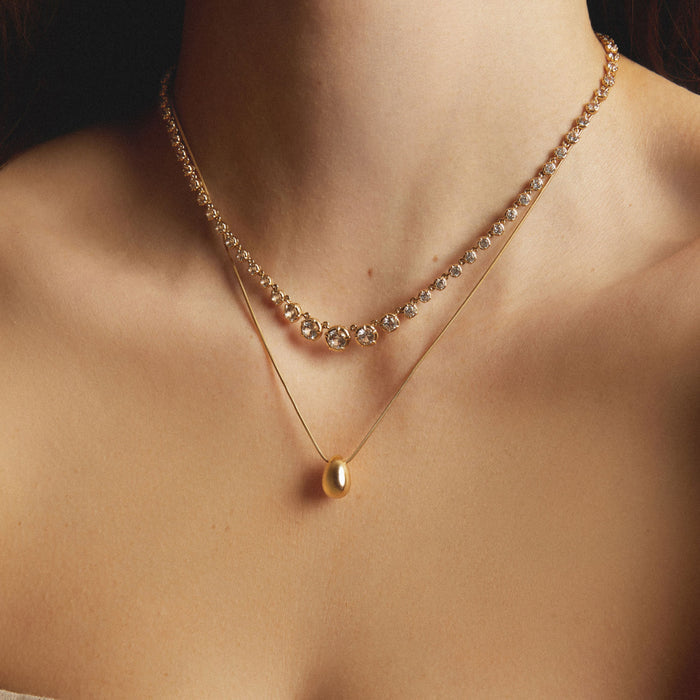 Model. One diamond tennis necklace and one gold pendant necklace stacked at different lengths on a woman.
