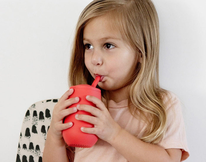 Child drinking at Ezpz Happy Cup & Straw in Coral - Available at www.tenlittle.com