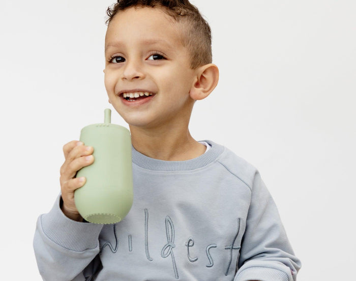 Child Holding Ezpz Happy Cup & Straw in sage - Available at www.tenlittle.com