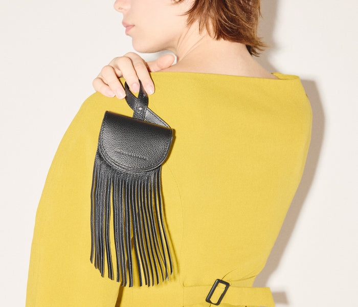 Black Joni Fringe Bag Charm by Freda Salvador hanging from a bag, showcasing leather fringe details and compact design.