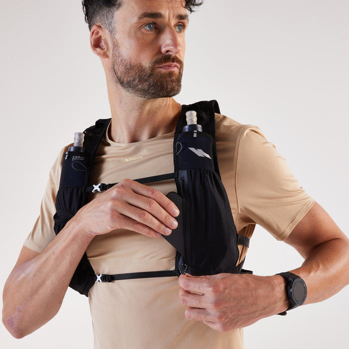 Man wearing a black running vest with hydration bottles on a plain background