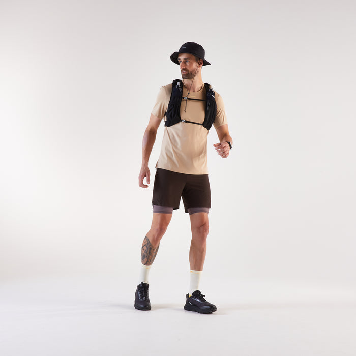 Man wearing a beige t-shirt, black shorts, and a black backpack on a white background