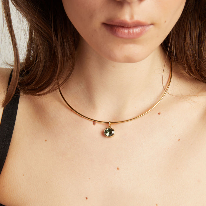 Model. Close up of a woman wearing a gold necklace with a green gemstone pendant.