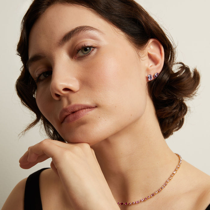 Close-up of a woman wearing a purple necklace and earrings against a neutral background. Model