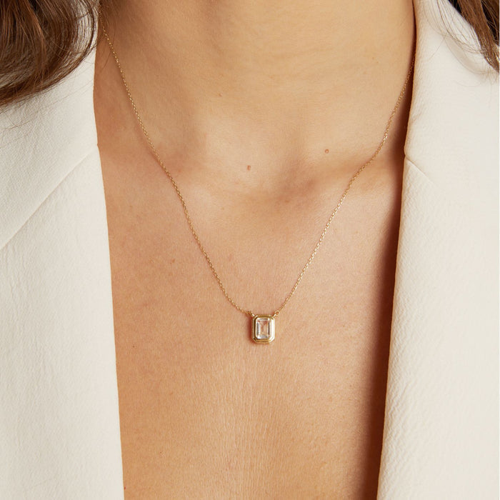 Model. Gold necklace with a pendant on a person wearing a white shirt