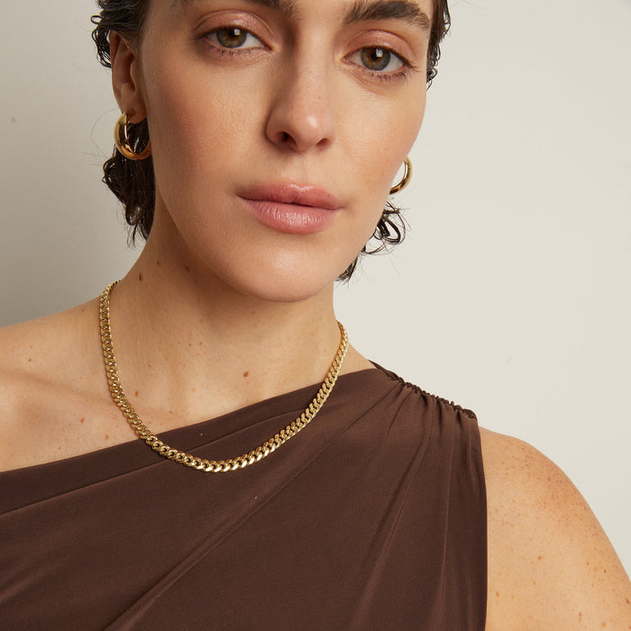 Model. Woman wearing a gold chain necklace and hoop earrings against a neutral background