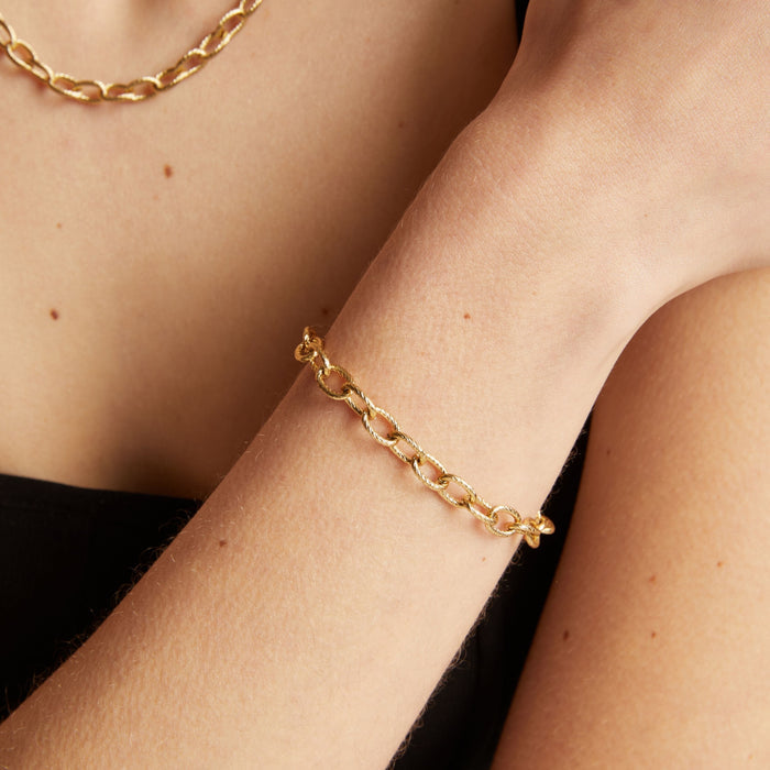 Model. Gold chain bracelet on a wrist with a neutral background.