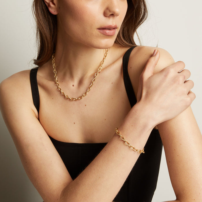 Model. Woman wearing a gold chain necklace and bracelet against a neutral background.
