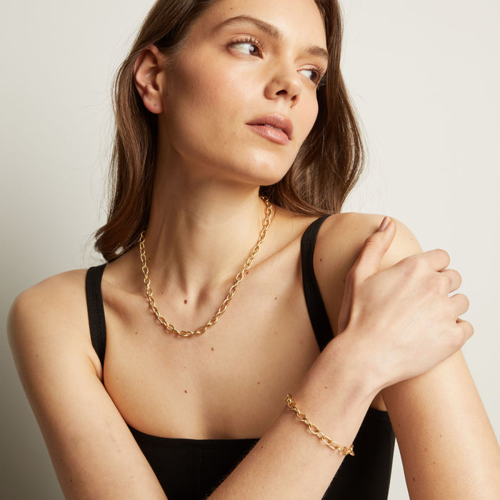 Model. Woman wearing a gold chain necklace and bracelet against a neutral background.