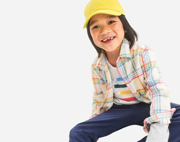 Child sitting wearing Primary Long Sleeve Button Down - Rainbow Flannel - Marshmallow / Rainbow Plaid. Available at www.tenlittle.com