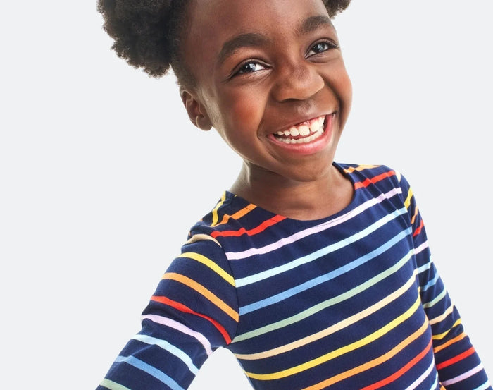 Child wearing Primary Long Sleeve Pocket Dress - Rainbow Stripe - Navy / Rainbow Stripe. Available at www.tenlittle.com