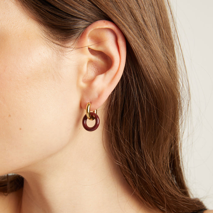 Model. Close up of an ear wearing a gold and maroon hoop earring.