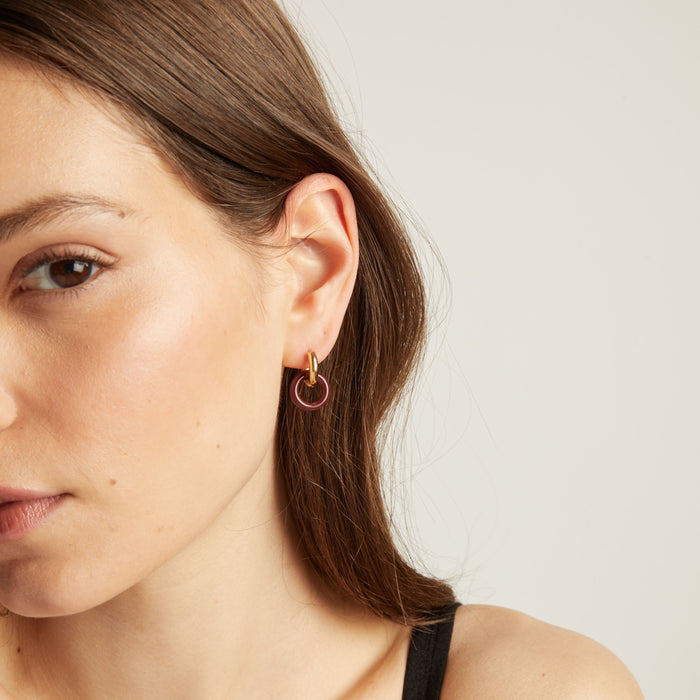 Model. Close up of a person wearing a gold and maroon hoop earring on a neutral background.