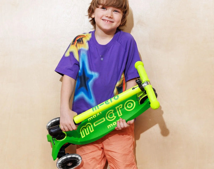 Child holding folded Micro Kickboard Maxi Deluxe Foldable LED Scooter - Neon Parrot Green. Available at www.tenlittle.com