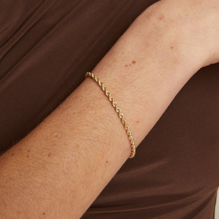 Model. Gold necklace and bracelet on a person wearing a brown top against a neutral background