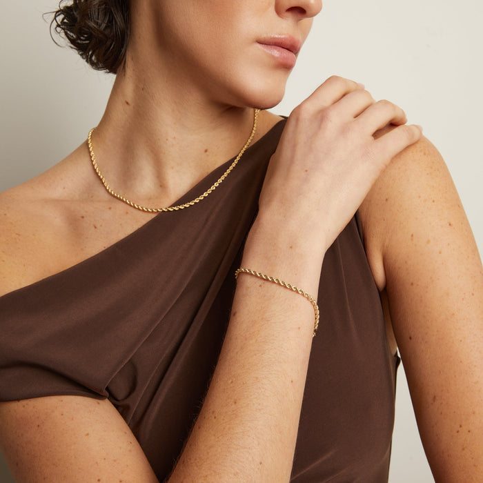 Model. Woman wearing a gold necklace and bracelet against a neutral background