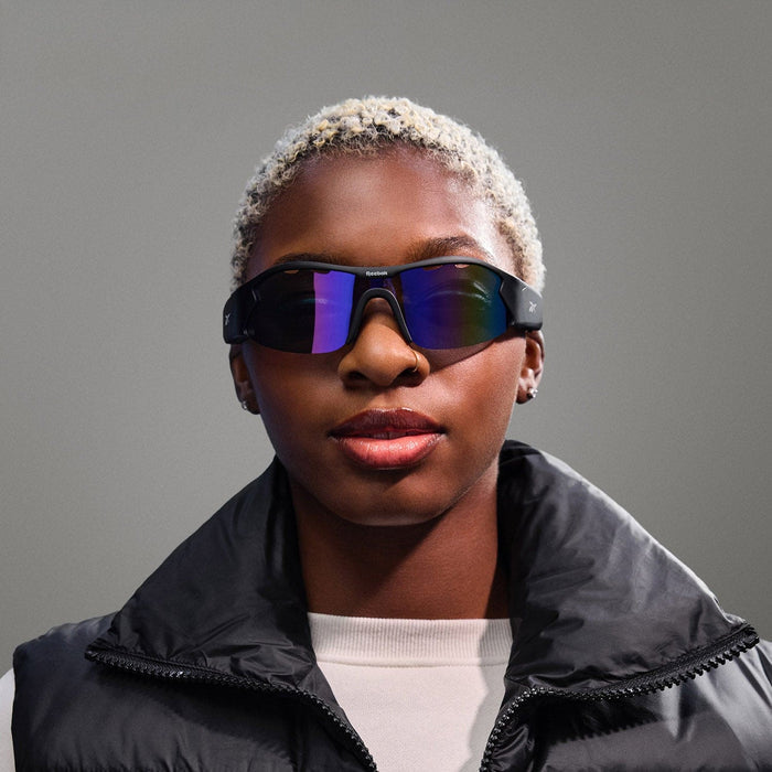 A woman enjoys her day in Reebok's Octane audio sunglasses and a sleek vest, effortlessly combining style and technology.
