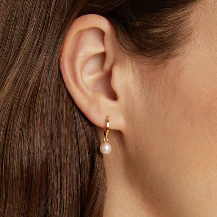 Model Close-up profile of a woman wearing a gold huggie earring with a dangling white pearl