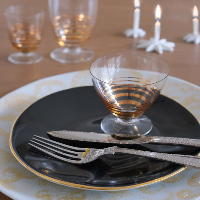 assiette noire et or avec couverts chics et verre dorés posés dessus