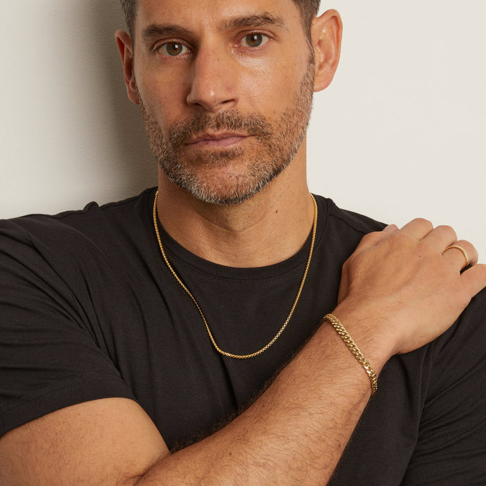 Man wearing a black shirt with gold jewelry against a plain background