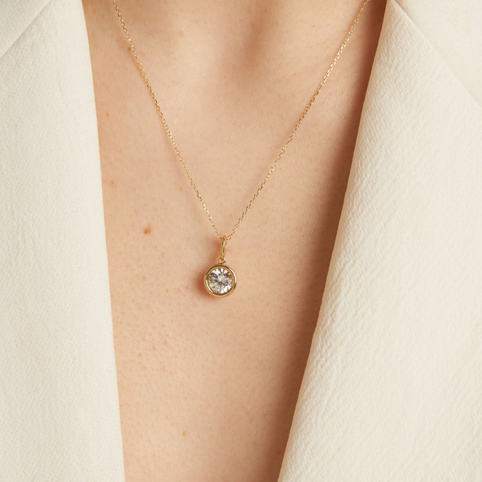 Model Gold necklace with a diamond pendant on a person wearing a white outfit.
