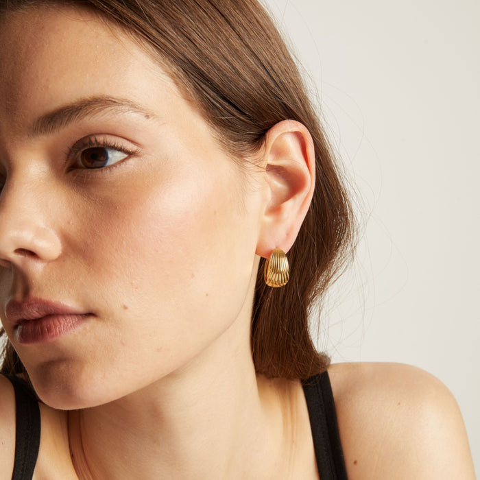 Model. Close up of a woman wearing gold hoop earrings with a neutral background.