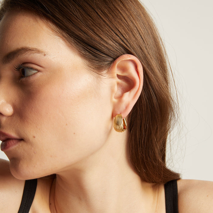 Model. Close up of a woman wearing gold hoop earrings with a neutral background.