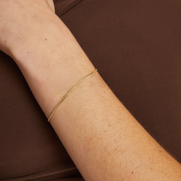 Model. Gold bracelet on a person's wrist against a brown background