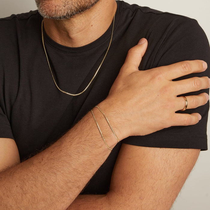 Man wearing gold jewelry including a necklace, bracelet, and ring on a neutral background