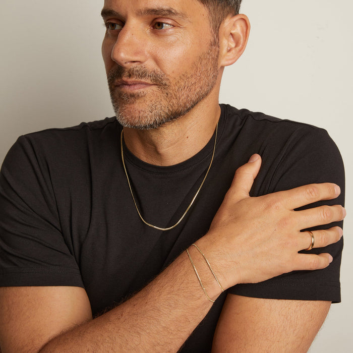 Model. Man wearing a black t-shirt with jewelry on a neutral background