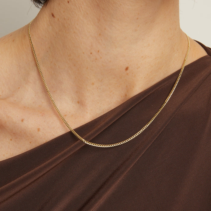 Model. Gold chain necklace worn by a person with a brown top